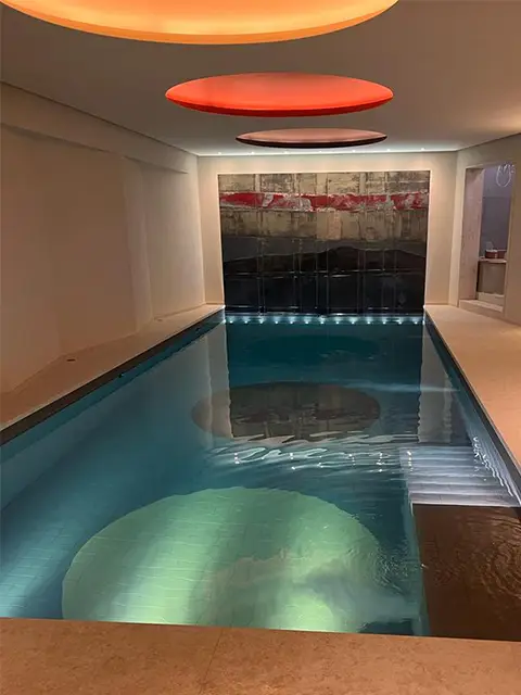 A small basement luxury swimming pool with futuristic ceiling lighting and circle patterns on the floor of the pool.