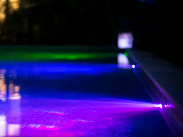 A nighttime shot of a swimming pool with different coloured underwater lights.