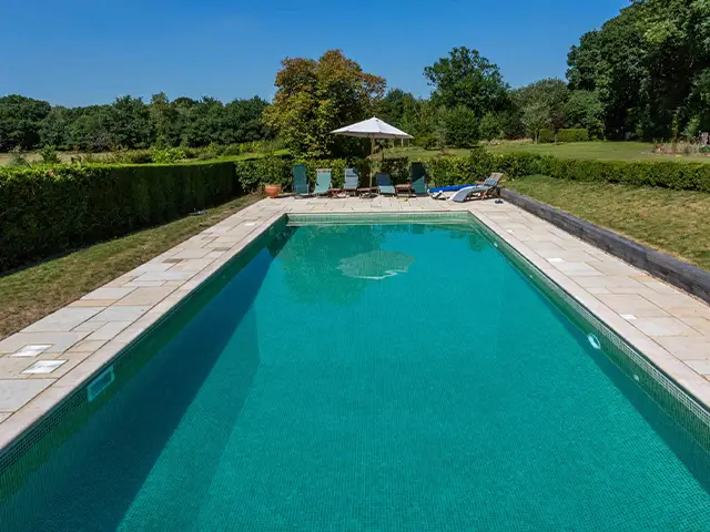 An outdoor home swimming pool set in a sunny countryside surrounding.