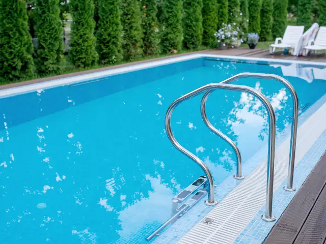 An outdoor deck-level swimming pool with a stainless steel pool ladder surrounded by decking.