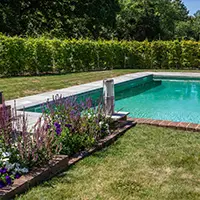 An outdoor heated swimming pool in a rural garden surrounded by hedges.