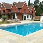 Outdoor swimming pool with house in background and patio surround.