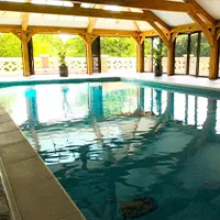 An indoor swimming pool with large wooden beams and glass folding doors.