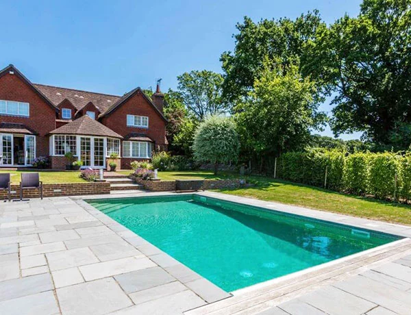 A large domestic outdoor swimming pool in the back garden of a large detatched house.