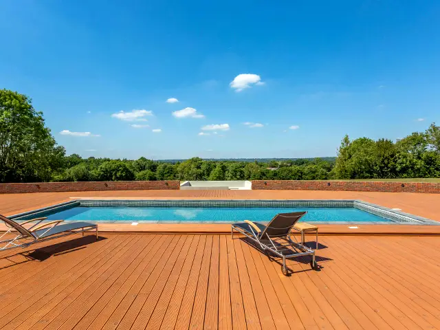 An outdoor countryside garden swimming pool with sunbeds set on a raised decking platform.