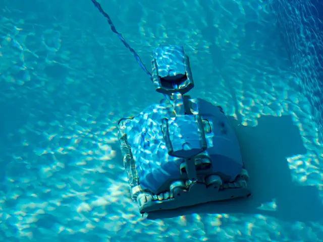 A pool cleaning robot at the bottom of a domestic swimming pool sucking up loose debris.