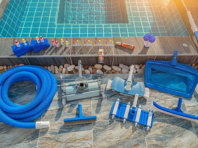 An array of pool cleaning and maintenance equipment laid out at the side of a domestic outdoor swimming pool.