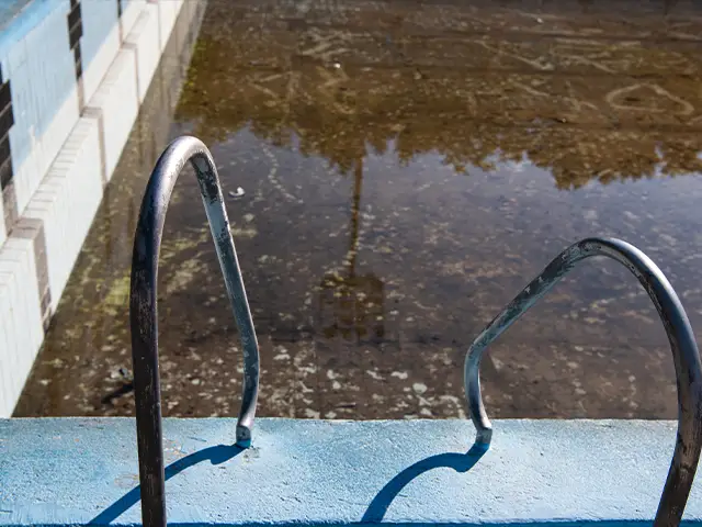 A run down swimming pool with a low water level and bent handlebars.