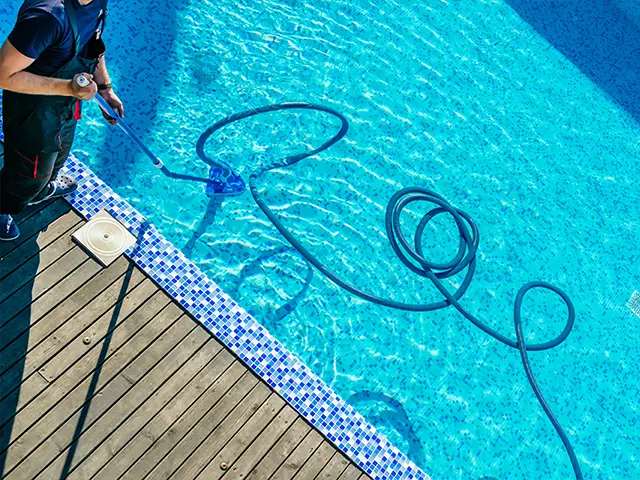 A swimming pool maintenance engineer vacuum cleaning a domestic swimming pool.