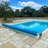 An outdoor swimming pool with patio slabs surround and a pool cover rolled up ready to protect the water from the elements.