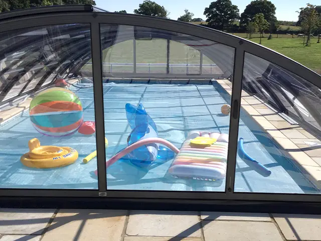 A glass swimming pool enclosure over a family garden pool.