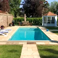 An outdoor garden swimming pool with sunbeds, a garden table and a pool vacuum by the side of the pool.