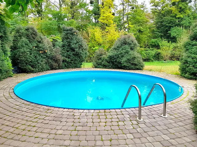 A round outdoor plunge pool in a back garden surrounded by bushes and trees.