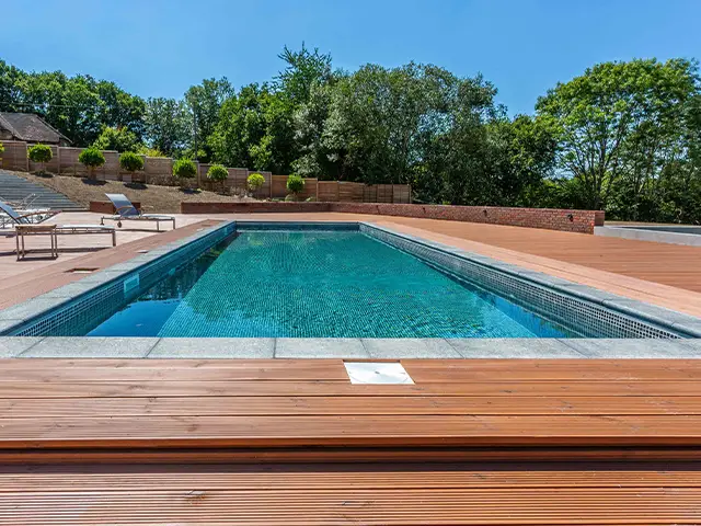 An outdoor countryside garden swimming pool with sunbeds set on a raised decking platform.