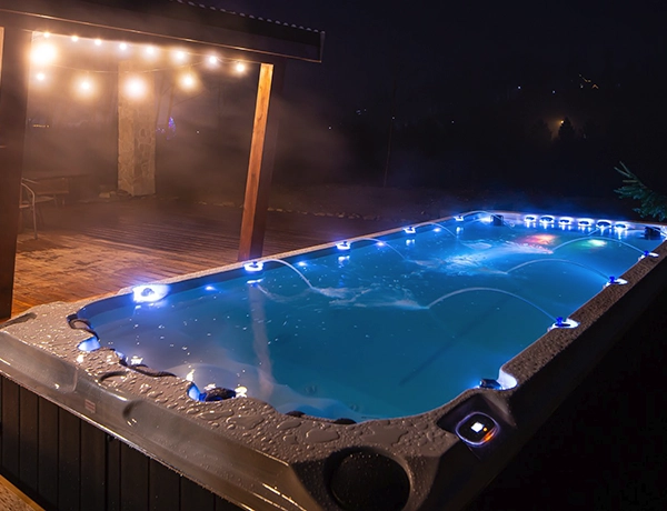 An swim spa with lights and jets of water surrounded by a wooden deck.